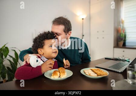 Father kissing son while having breakfast at home Stock Photo