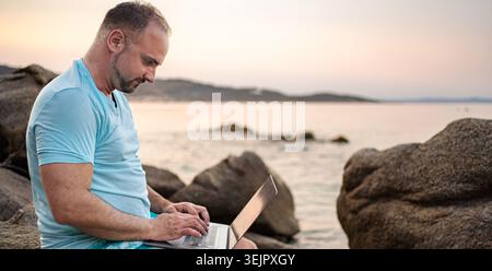 Man working on laptop beach during summer sunset Stock Photo