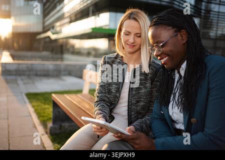 Diverse businesswomen collaborating outdoors using digital tablet Stock Photo
