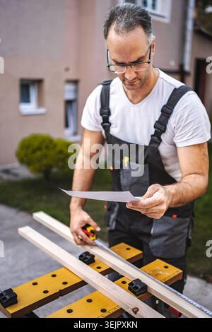 Mature male carpenter measuring wooden plank outdoors Stock Photo