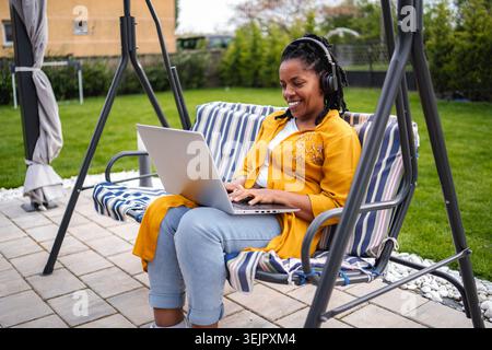 Woman working remotely from home on garden swing Stock Photo