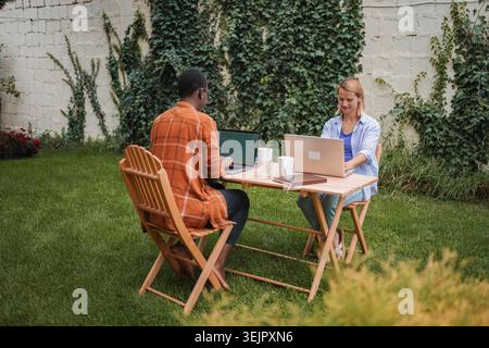 Two young professionals working remotely in a garden using laptops Stock Photo