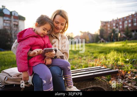 Mother and daughter using phone together in park Stock Photo