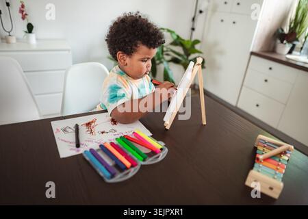 Toddler drawing on easel with colorful markers at home Stock Photo
