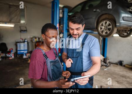 Two mechanics using a tablet in a car repair shop Stock Photo