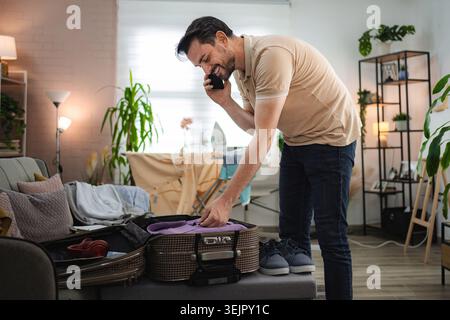 Man talking on the phone while packing suitcase at home Stock Photo