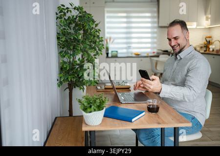 Freelance man working from home using laptop and smartphone Stock Photo