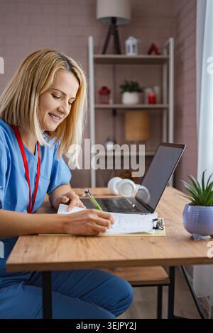 Female Doctor Working From Home Taking Notes and Smiling Stock Photo