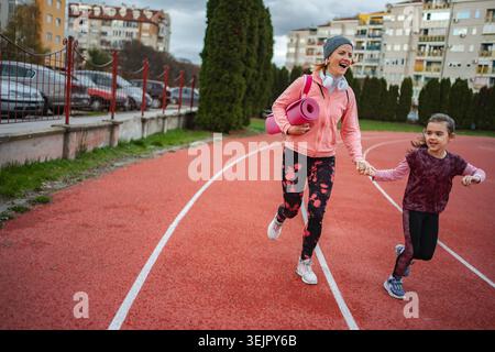 Mother and daughter running on track holding hands Stock Photo