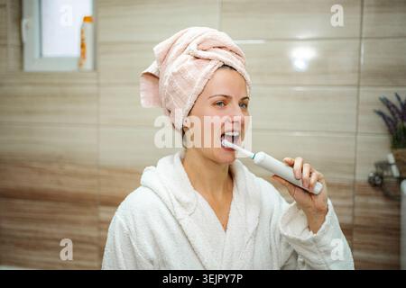 Woman brushing teeth with electric toothbrush during morning routine Stock Photo