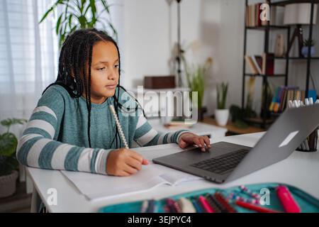 Girl studying homework at desk using laptop for remote learning Stock Photo