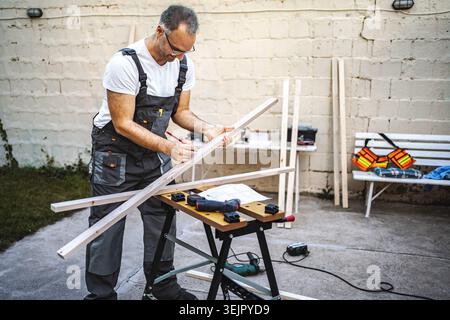 Mature male carpenter measuring wooden plank outdoors Stock Photo