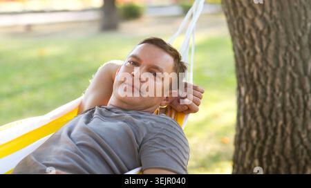 Portrait of mature smiling man looking into the camera lying in a hammock in the garden on a summer day Stock Photo