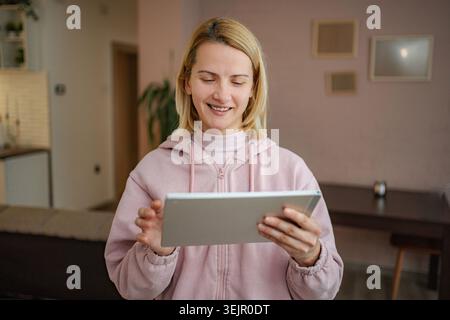 Young adult woman using digital tablet at home smiling Stock Photo