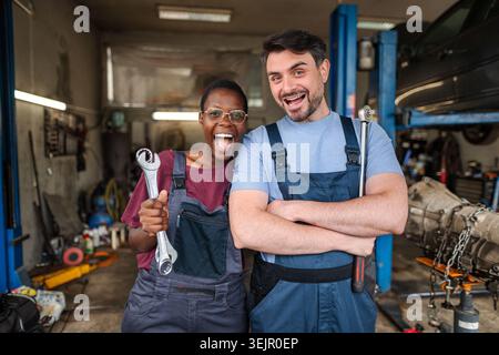 Two happy mechanics smiling at the camera in a car repair shop Stock Photo