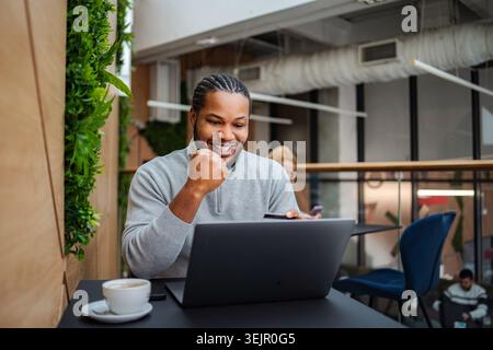Happy black man celebrating success using laptop in cafe Stock Photo