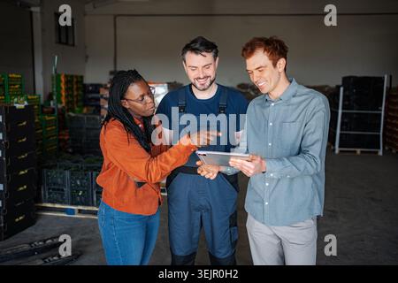 Diverse team of logistics professionals collaborating on inventory management using technology in a warehouse Stock Photo