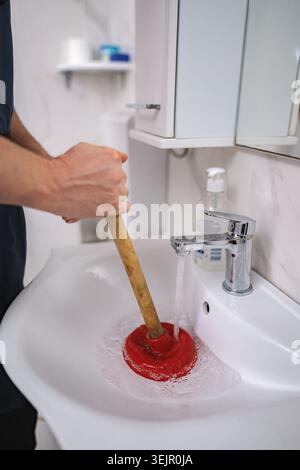 Plumber using plunger in bathroom sink Stock Photo