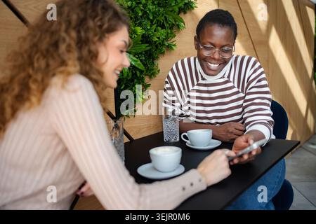 Diverse friends enjoying coffee sharing content on smartphone Stock Photo
