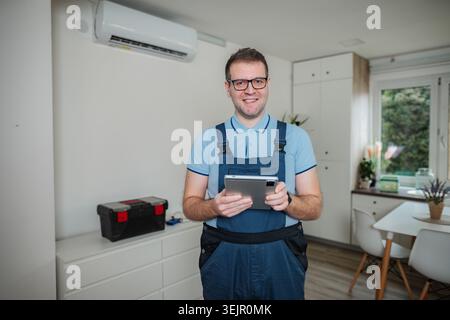 HVAC technician holding digital tablet checking apartment air conditioner Stock Photo