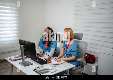 Two diverse female nurses smiling and laughing while working at a computer in an office Stock Photo