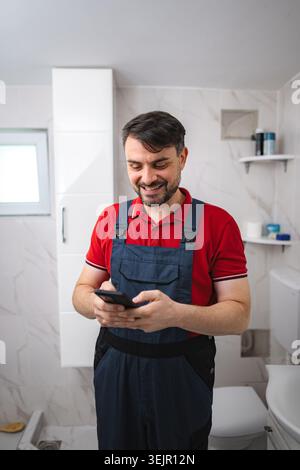 Plumber smiling and using smartphone in bathroom during house renovation Stock Photo