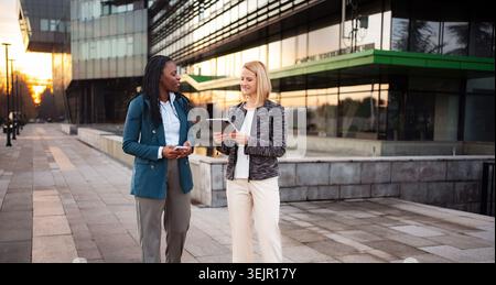Diverse businesswomen walking, discussing work with tablet and smartphone Stock Photo