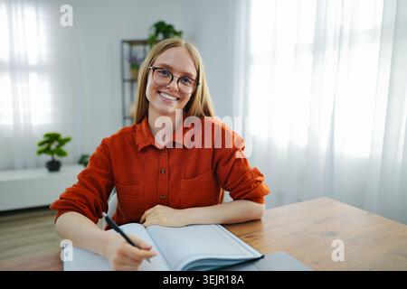 Woman smiling while writing in a notebook in a bright room Stock Photo