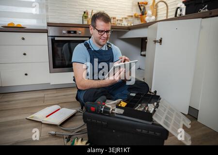 Plumber using digital tablet repairing pipe under kitchen sink Stock Photo