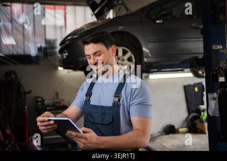 Mechanic Smiling and Using Digital Tablet in Auto Repair Shop Stock Photo