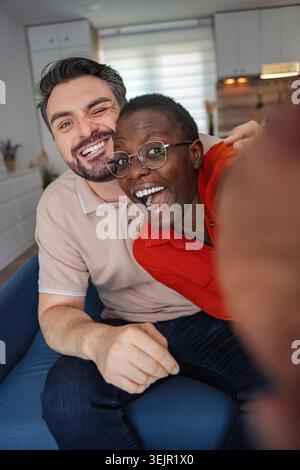 Happy multiethnic couple taking a selfie on the sofa at home Stock Photo