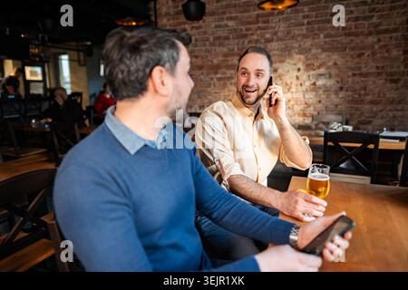 Friends socializing at pub while using technology and drinking beer Stock Photo