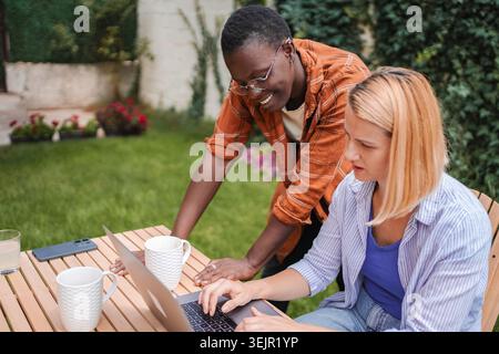 Two female colleagues working on a laptop in the garden Stock Photo