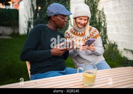 Diverse women spending time together using smartphones outdoors Stock Photo