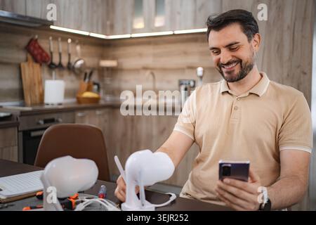 Technician smiling and using smartphone while installing smart home devices in a kitchen Stock Photo