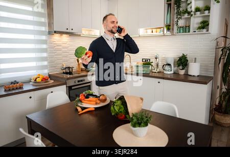 Man talking on phone holding vegetables in kitchen Stock Photo