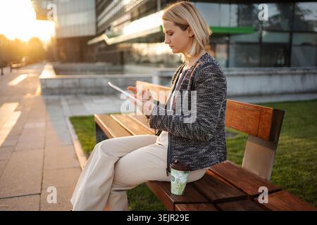 Businesswoman using digital tablet on bench enjoying sunset Stock Photo