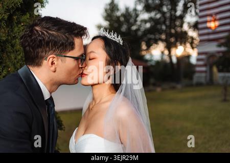 Interracial wedding couple kissing outdoors at sunset Stock Photo