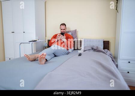 Man relaxing in bed using smartphone in modern bedroom Stock Photo