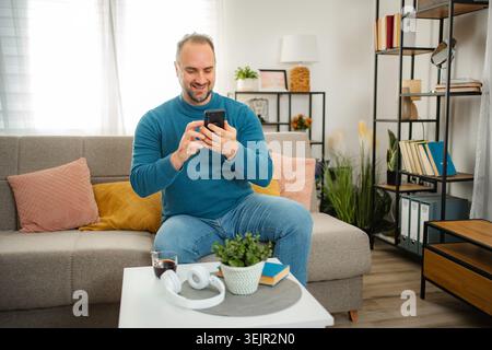 Man relaxing on sofa using smartphone at home Stock Photo