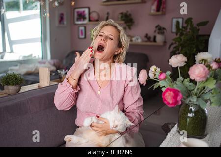 Adult woman yawning holding sleepy white cat Stock Photo
