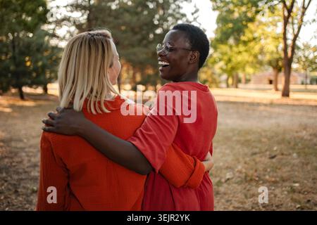 Two friends hugging and laughing in a park Stock Photo