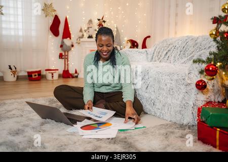 Adult woman working remotely, analyzing documents and using laptop during Christmas Stock Photo