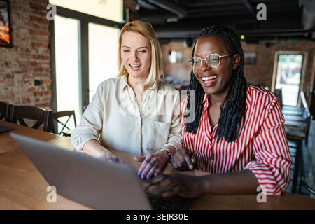 Diverse women collaborating on laptop in a casual cafe Stock Photo