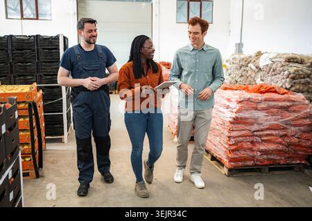Diverse workers discussing logistics in produce warehouse with digital tablet Stock Photo