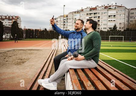 Male friends sitting on stadium benches taking selfie Stock Photo