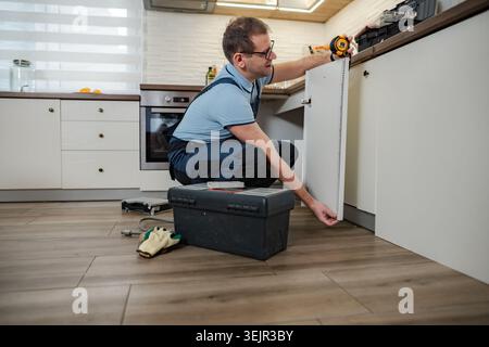Handyman installing kitchen cabinet door, using measuring tape Stock Photo