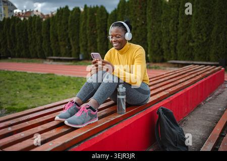African American woman relaxing on bench using smartphone Stock Photo