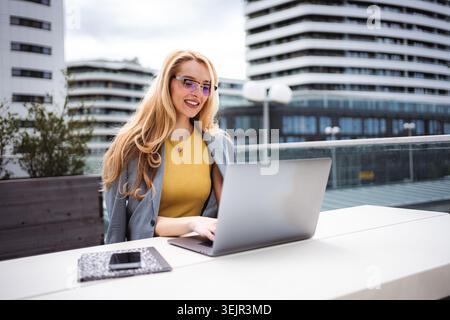 Businesswoman working on laptop on urban building rooftop Stock Photo