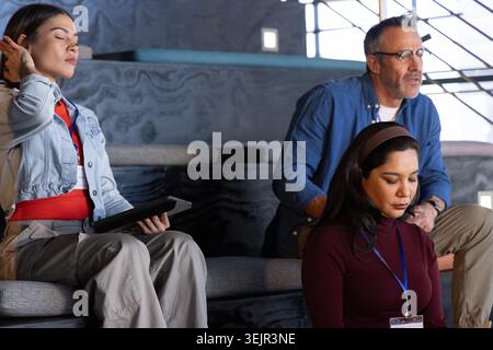 Diverse coworkers front row woman sitting on tiered seats in lecture hall holding tablet and badges. Attendees, auditorium, conf Stock Photo